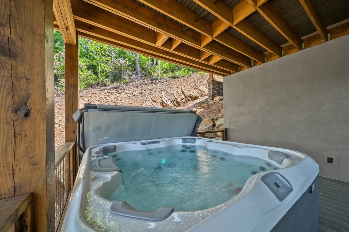 A cozy hot tub space with wooden beams and windows looking out onto surrounding trees, blending indoor comfort with the tranquility of nature. The setting is intimate, perfect for unwinding after an active day or hosting small group wellness sessions.