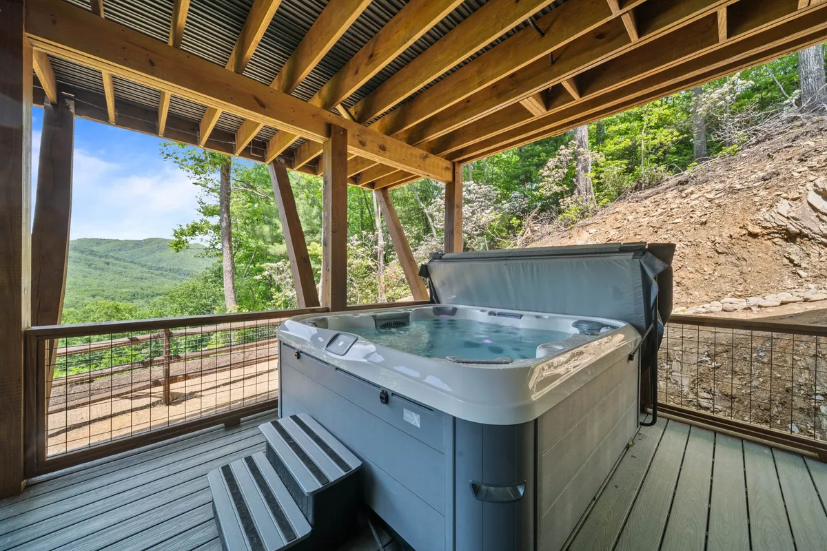 This image spotlights a private hot tub positioned on a spacious wooden deck, with a sweeping view of the surrounding mountains. The wooden structure, open sky, and tranquil setting evoke relaxation and a sense of luxury. Subtle details like the soft light and natural scenery suggest both daytime enjoyment and evening stargazing.