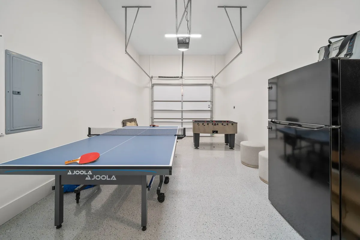 This image features a game room equipped with both a ping pong table and a foosball table, as well as a black refrigerator in the background. The scene is lively and energetic, emphasizing the playful and social atmosphere of the entertainment retreat.