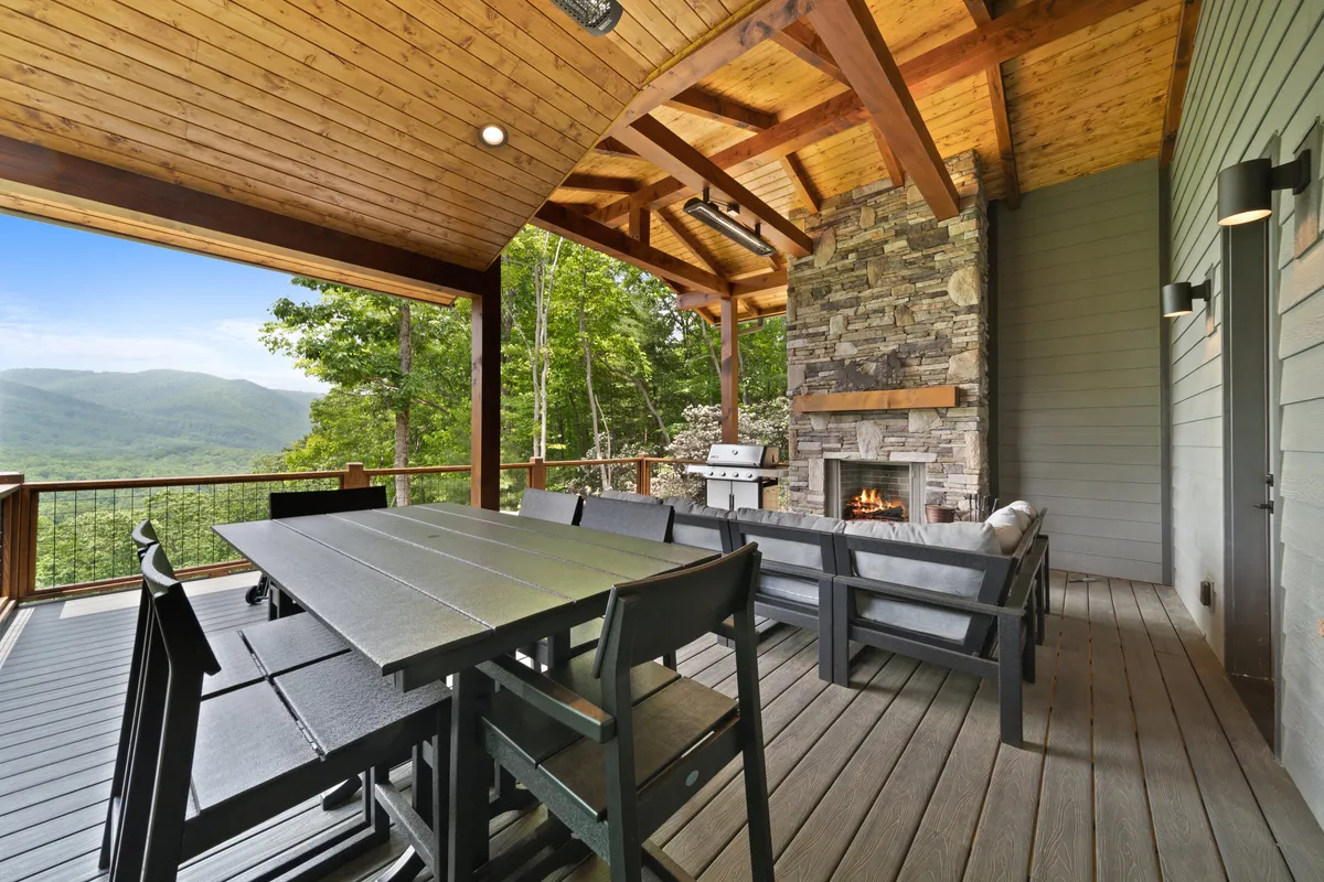 A spacious outdoor dining area with a stone fireplace, large table for group meals, and panoramic mountain views creates an idyllic setting for social gatherings, barbecue dinners, and intimate evenings by the fire.