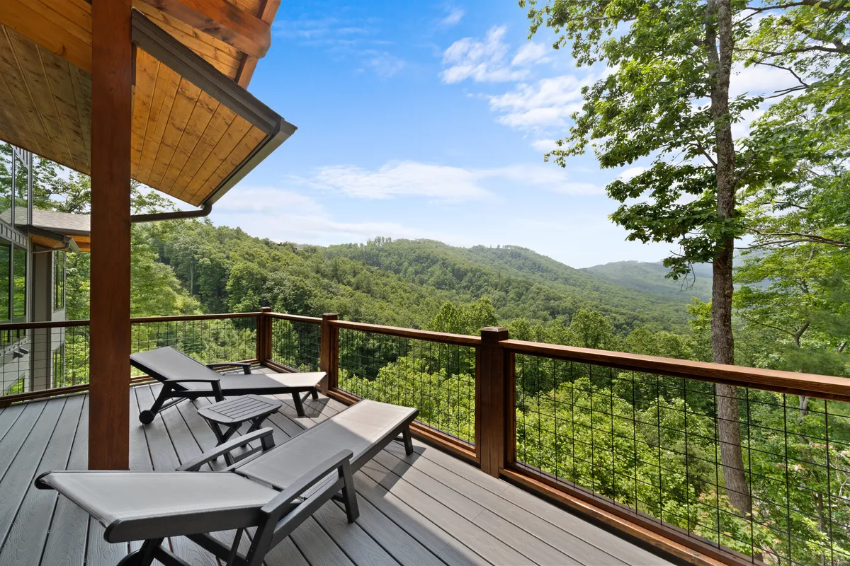 A wooden deck with lounge chairs facing panoramic mountain views, inviting guests to sunbathe, read, or simply soak in the natural beauty. The wood railing and open-air setting emphasize the seamless blend between the home’s interior and the great outdoors.