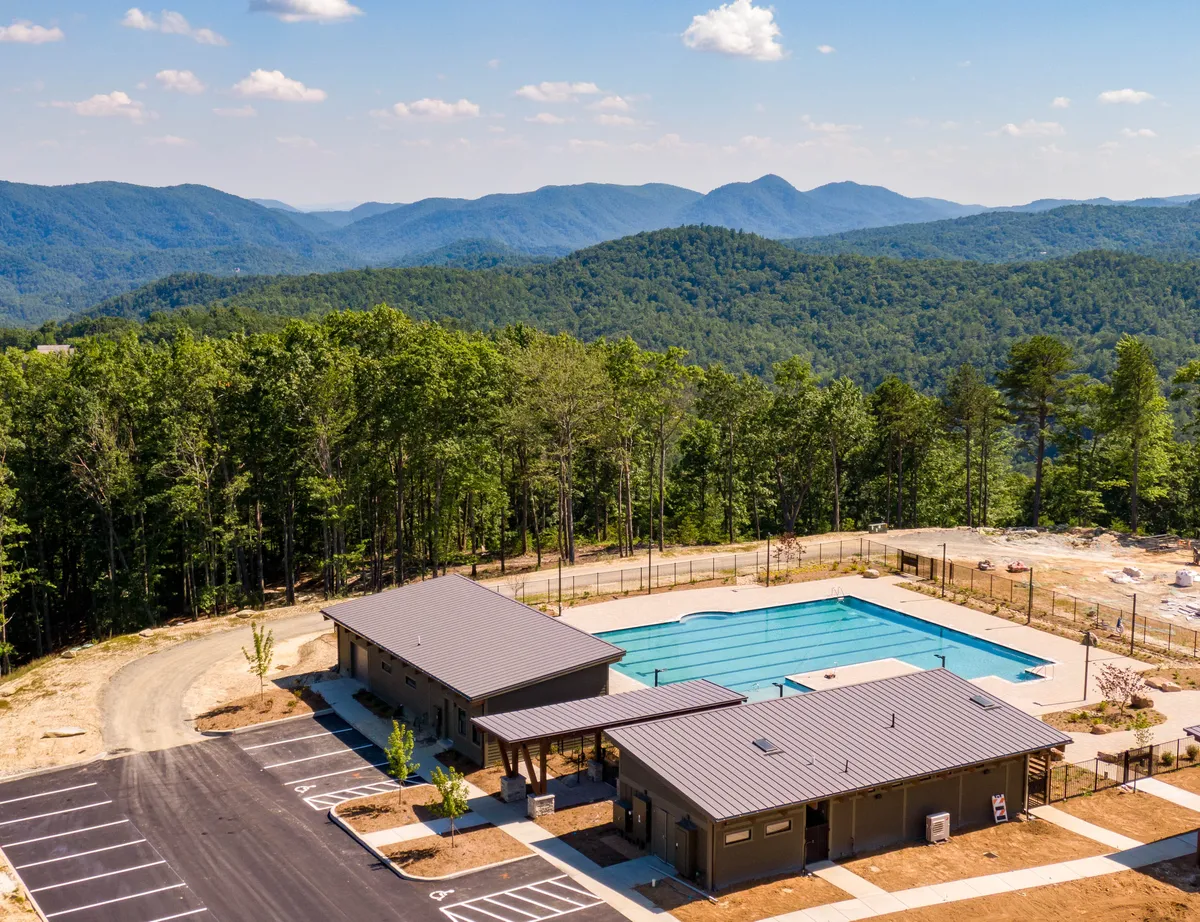 A relaxing swimming pool is set against the backdrop of surrounding mountains and recreational buildings. The setting implies opportunities for recreation, relaxation, and socializing after a day on the trails or courts.