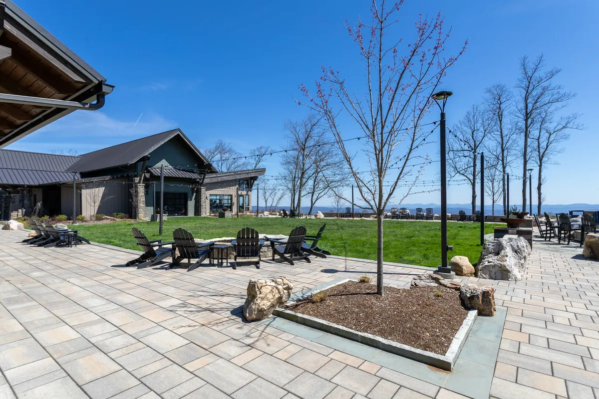 An inviting patio seating area is surrounded by beautifully landscaped gardens, with a modern building in the background and distant mountains on the horizon. The space encourages relaxation, gathering, and soaking up nature. The scene captures the transition between indoor and outdoor environments and hints at opportunities for reflection and group connection.